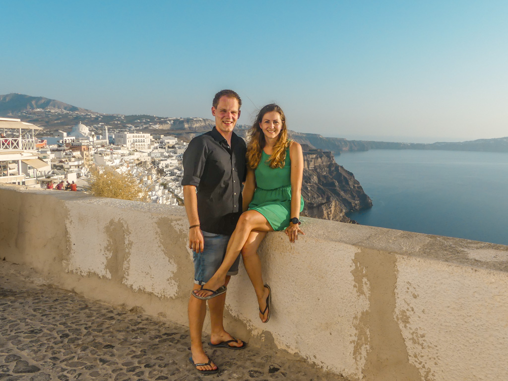 Pärchen sitzt auf Mauer mit Ort Fira auf Santorini im Hintergrund